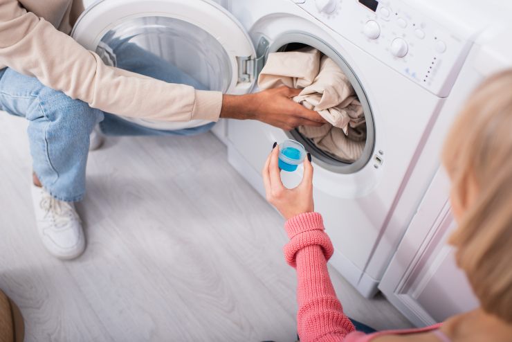 Donna che inserisce del liquido azzurro nella lavatrice - foto Depositphotos - Solofinanza.it