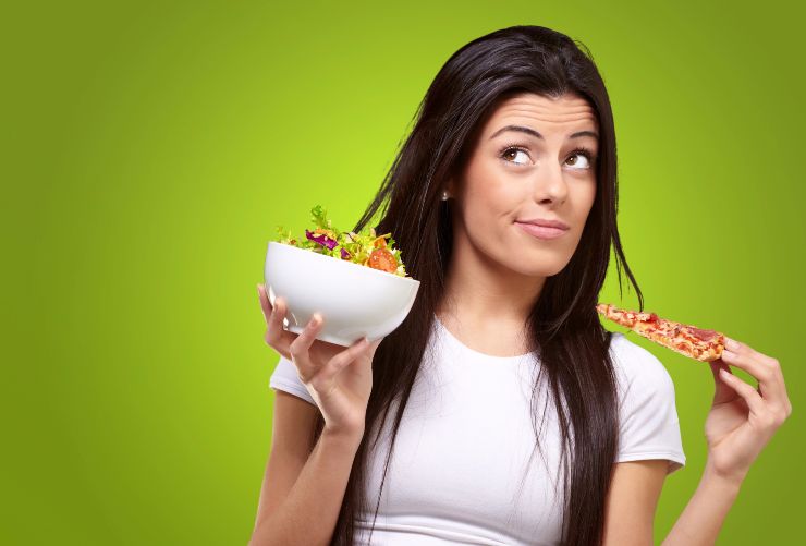 Ragazza indecisa se mangiare insalata o pizza - foto Depositphotos - Solofinanza.it